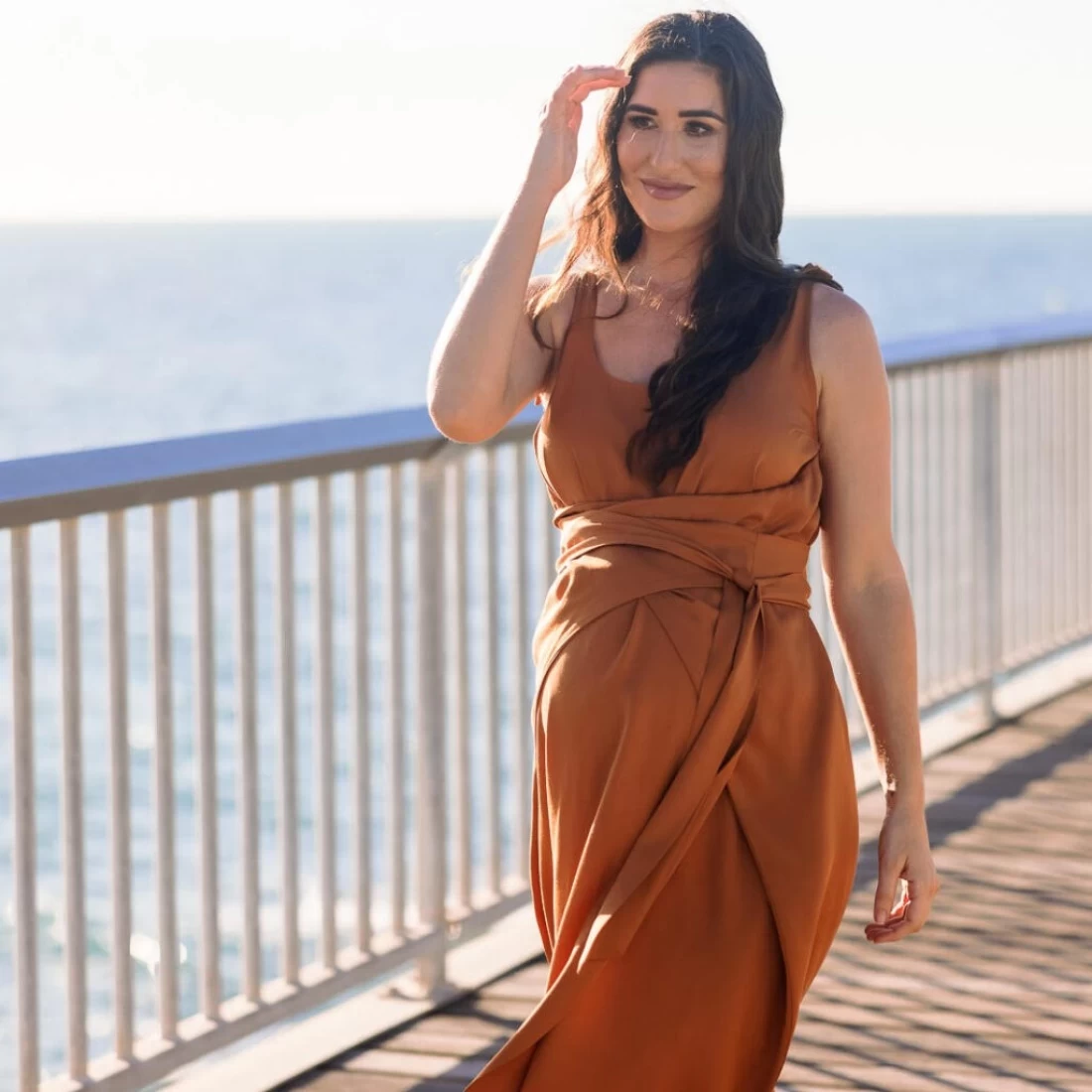 Mum standing on a terrace overlooking the sea, wearing a Toots & Co maternity outfit, combining comfort with coastal style.