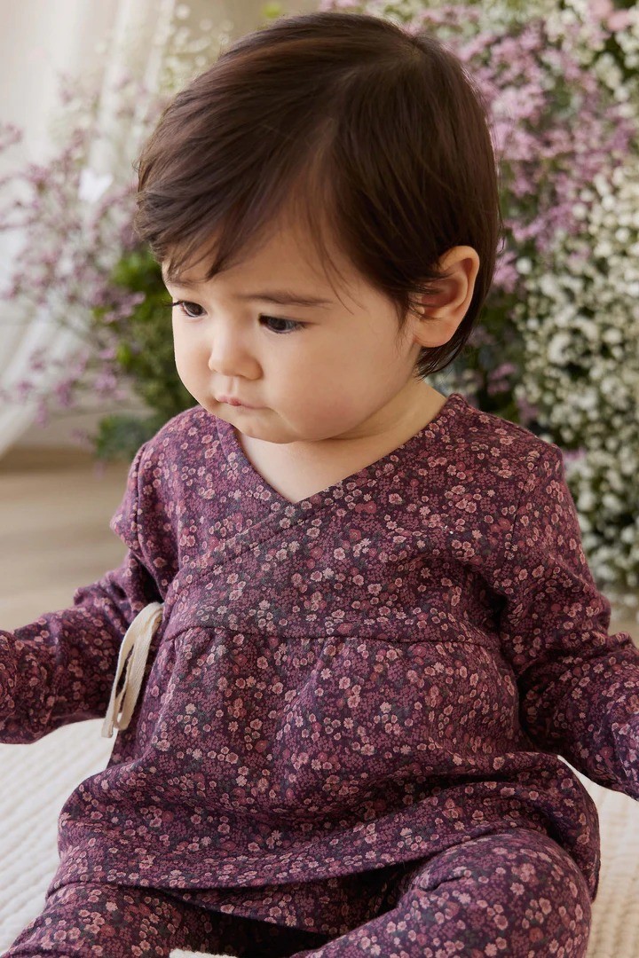 A little baby wearing a purple dress and leggings by Jamie Kay