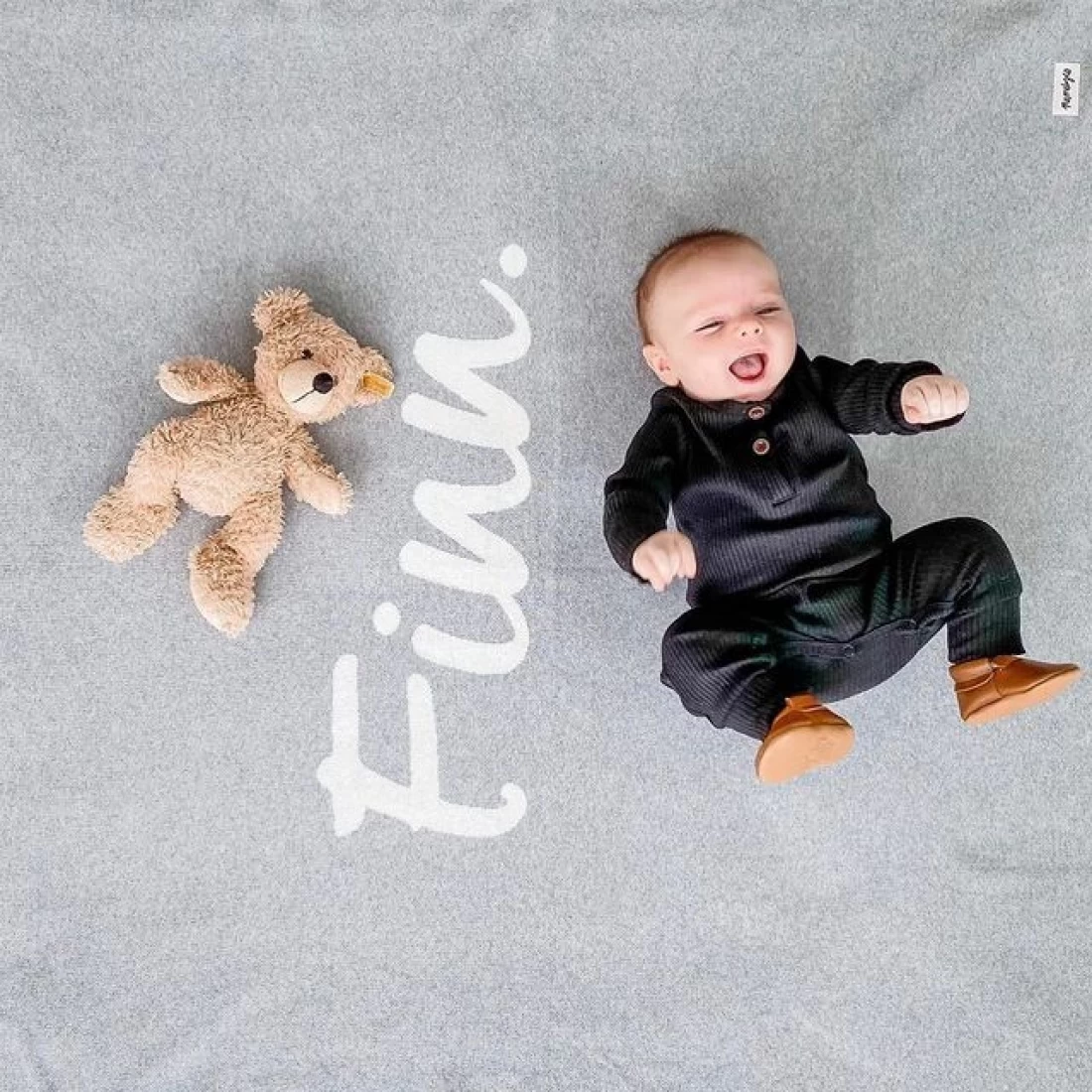 Top shot of a baby lying on a bed with a personalised sheet featuring the best baby boy name.