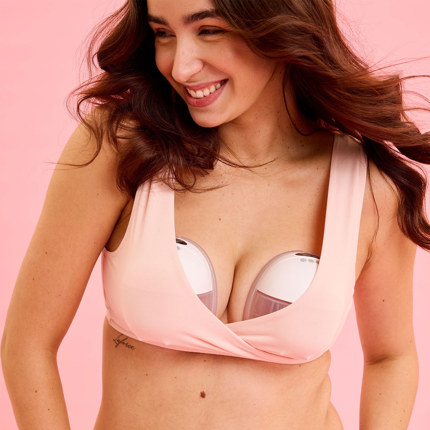 Mother expressing milk with New Beginnings wearable breast pump in a nursing bra on a pink background