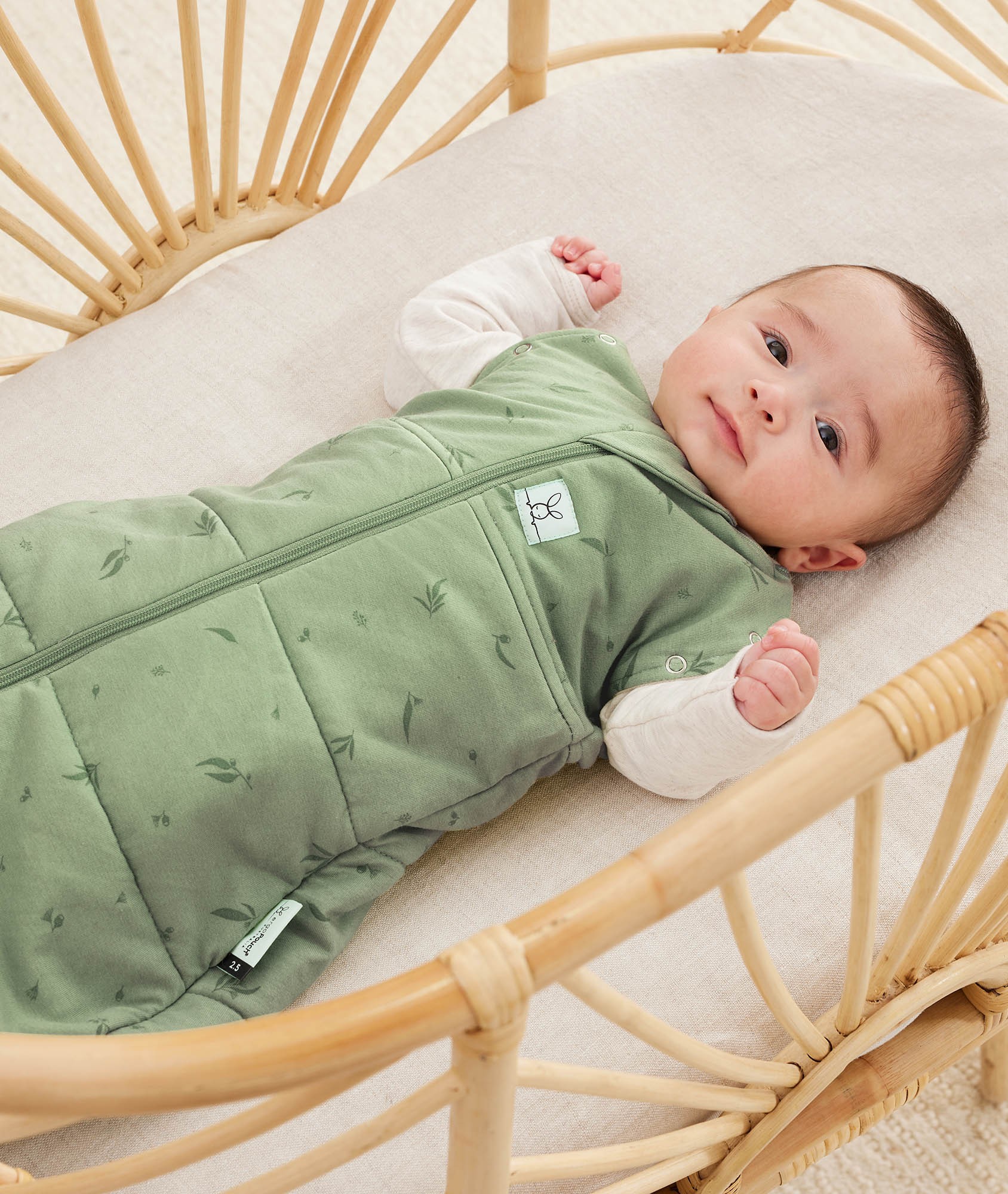Australian newborn resting in a wooden bassinet dressed in a soft green baby swaddle bag