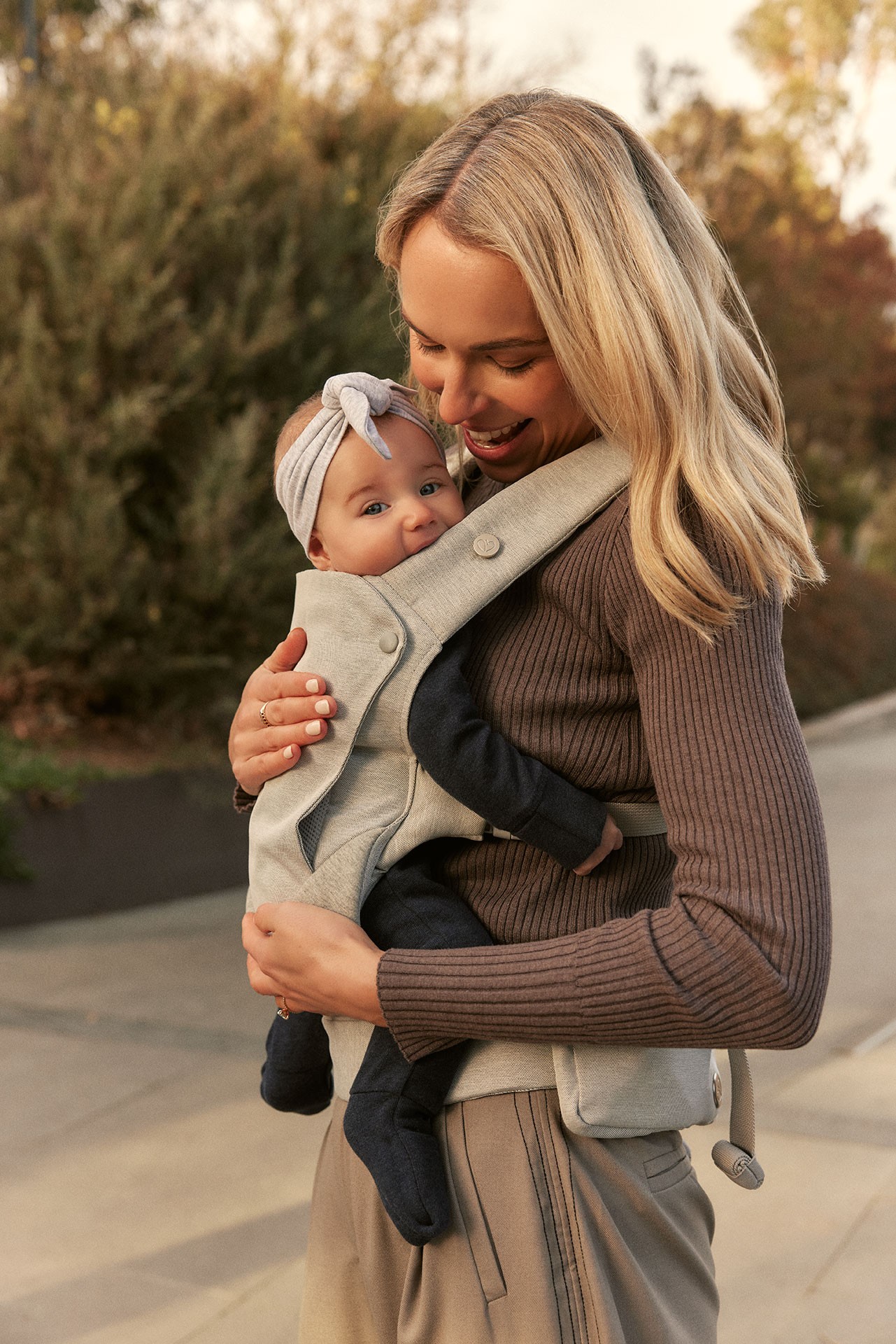 Side view close up of a mum joyfully carrying her baby in the best baby carrier Australia with a unique body hugging fit while heading to the park