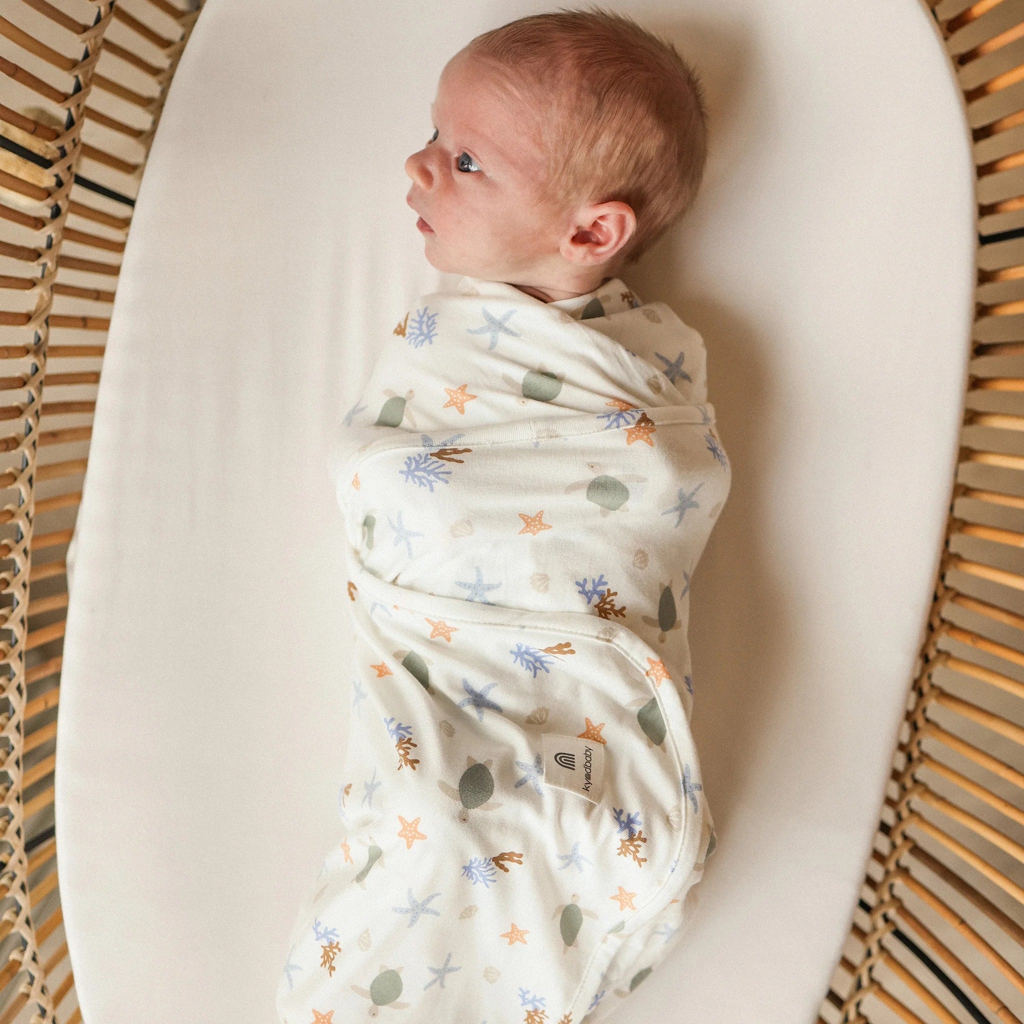 A baby in a stretch swaddle by KyndBaby, one of our newborn essentials recommendations