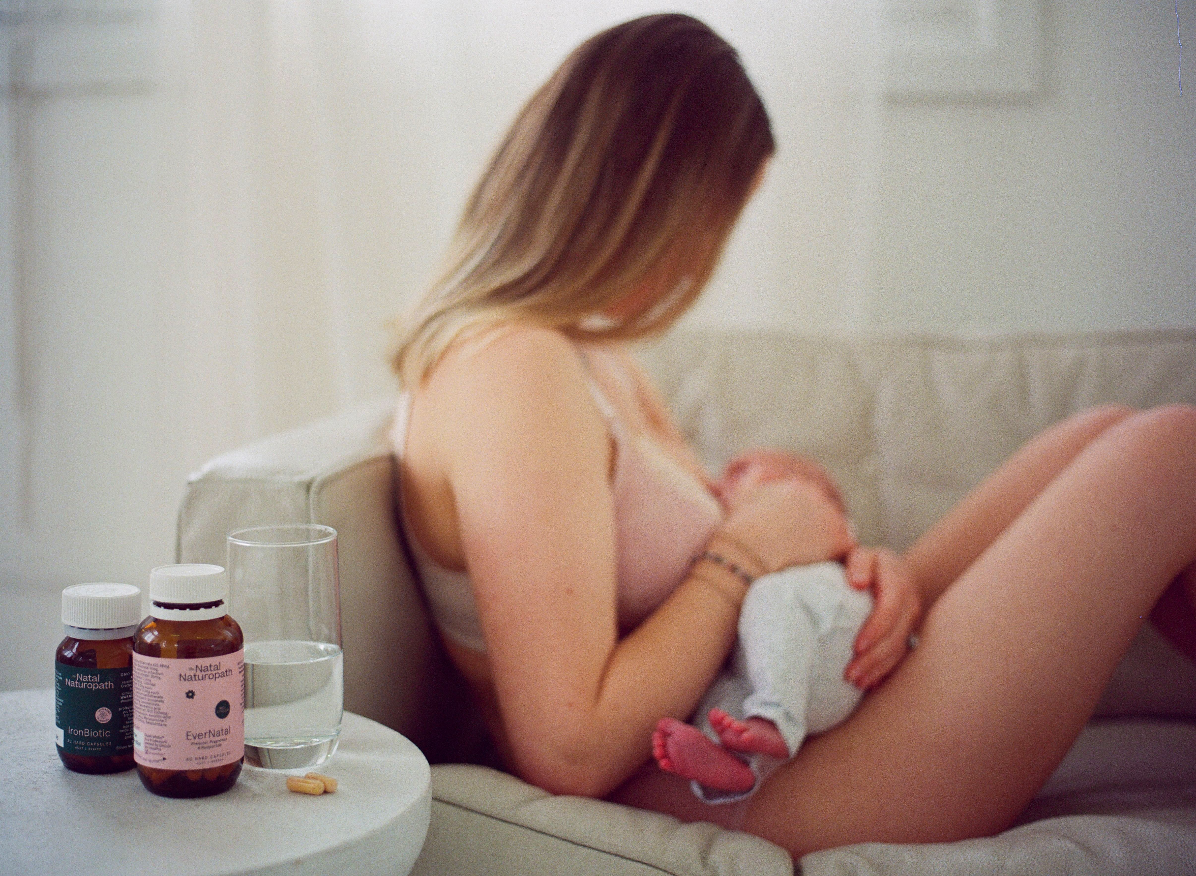Natal Naturopath EverNatal prenatal vitamin bottles in foreground with breastfeeding mum blurred behind