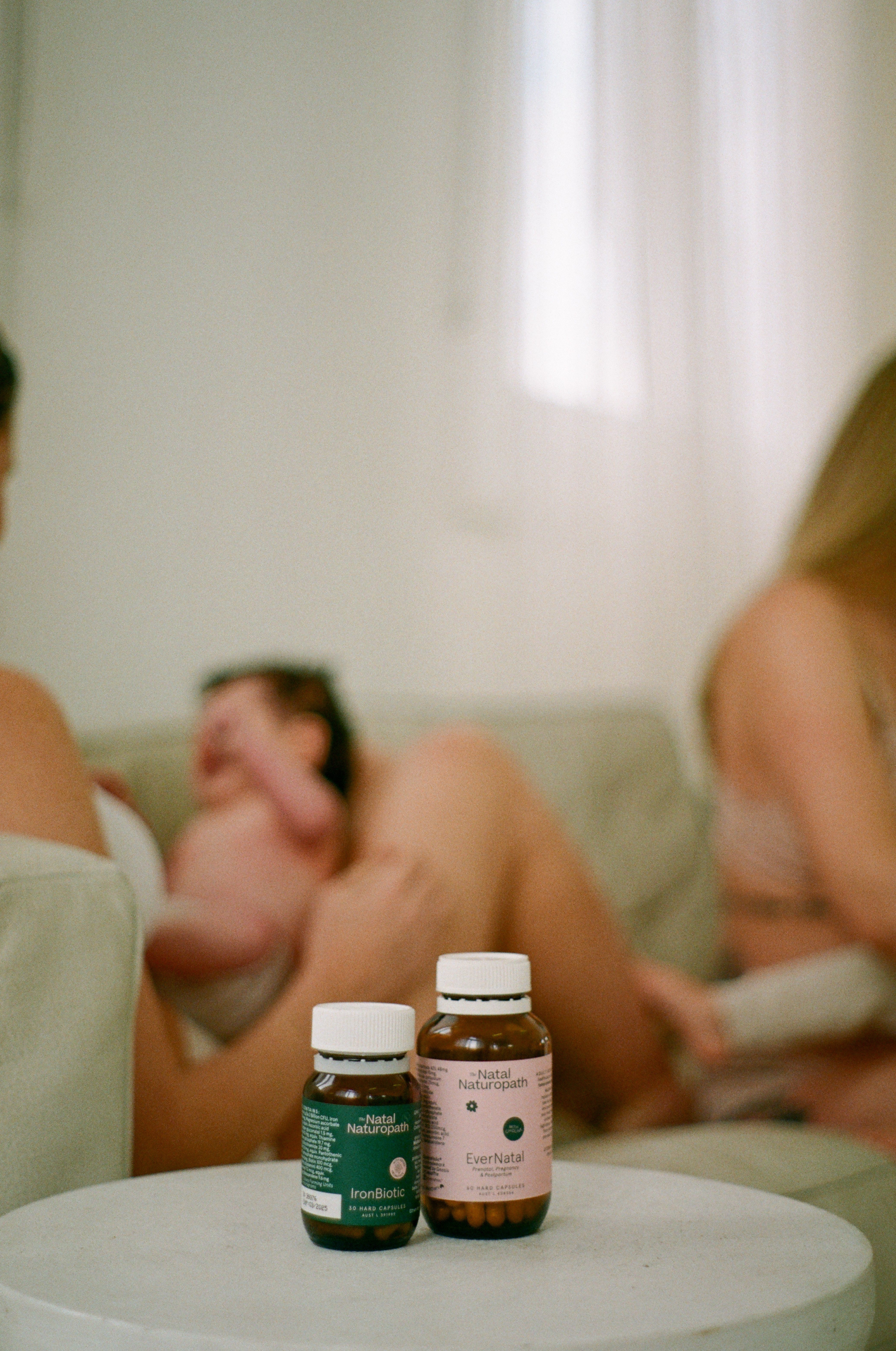 Two Natal Naturopath EverNatal supplement bottles in focus with mums chatting behind