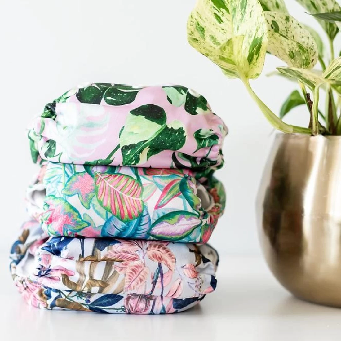 Stack of cloth nappies from the best baby brand on a white background with a vase of green plant.