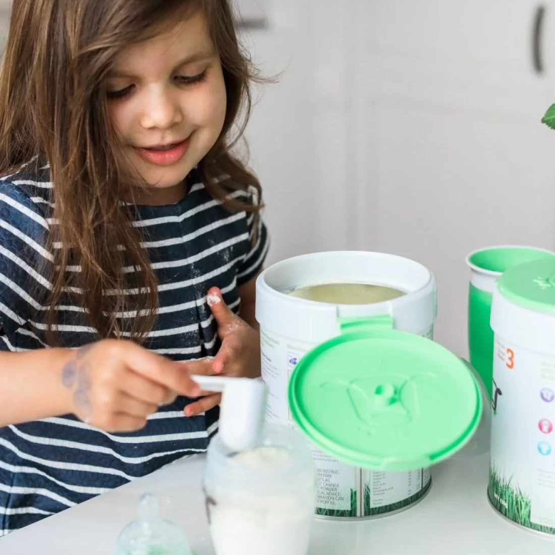 Baby girl scooping milk into a glass with support from the best baby brand.