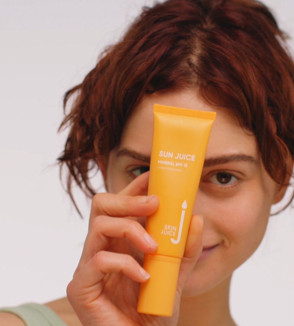 Pregnant woman’s face in background as she holds Sun Juice tinted moisturiser, safe for pregnancy skin condition care.