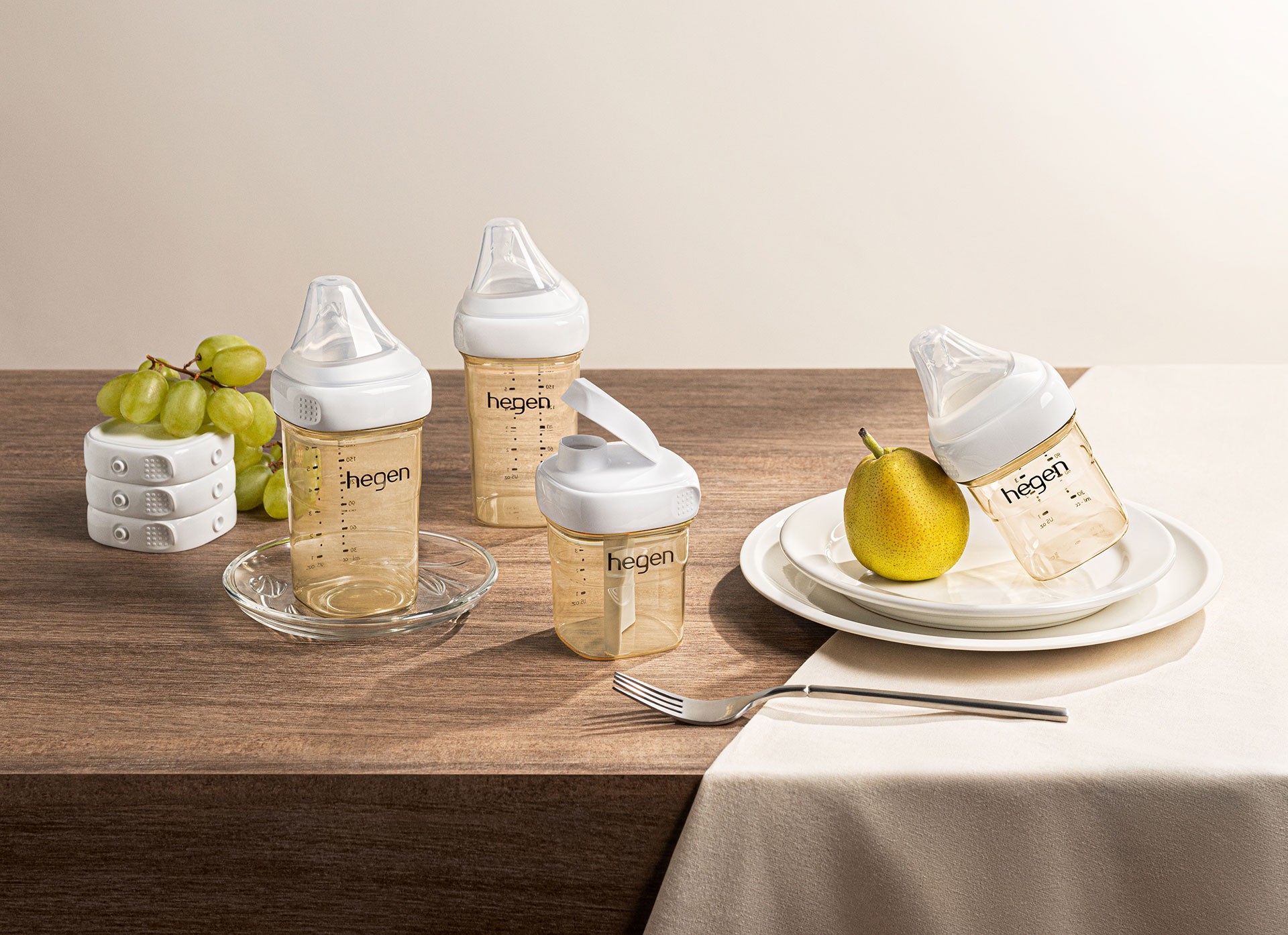 Best baby bottles by Hegen lined up on a dining table featuring different spouts and lids for feeding and drinking stages