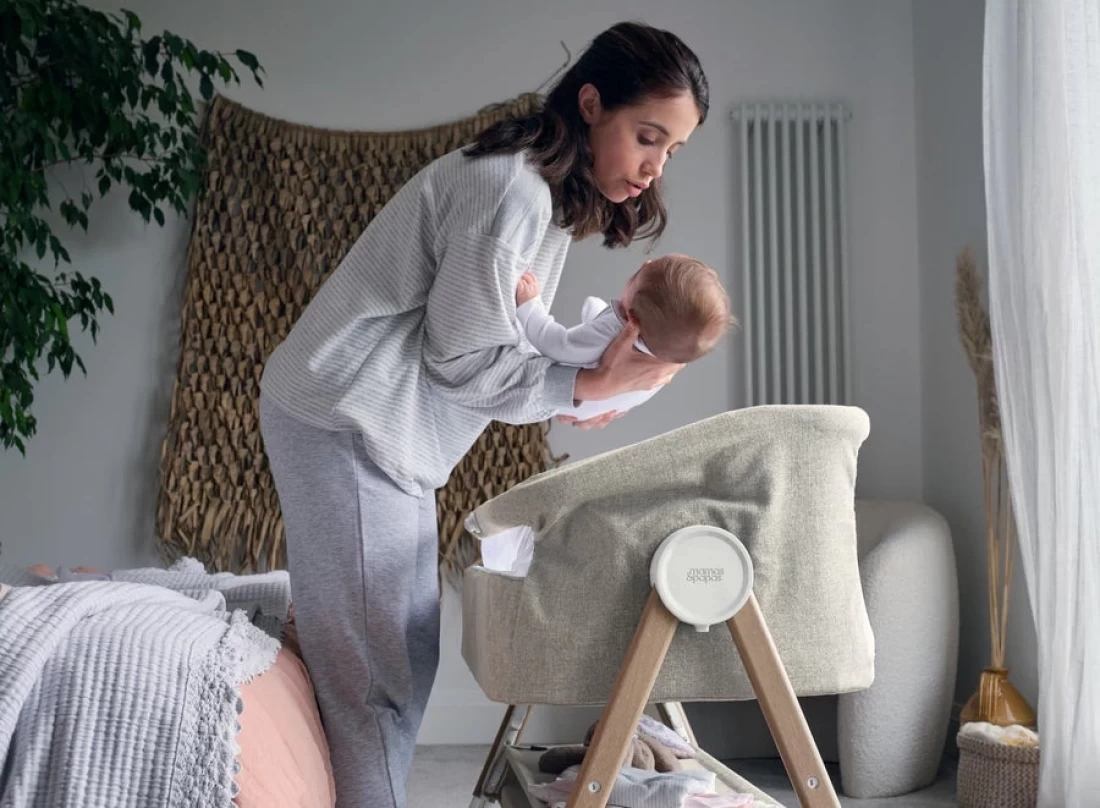 Mum gently putting her baby into the crib inside a beautifully styled Mamas and Papas Nursery.