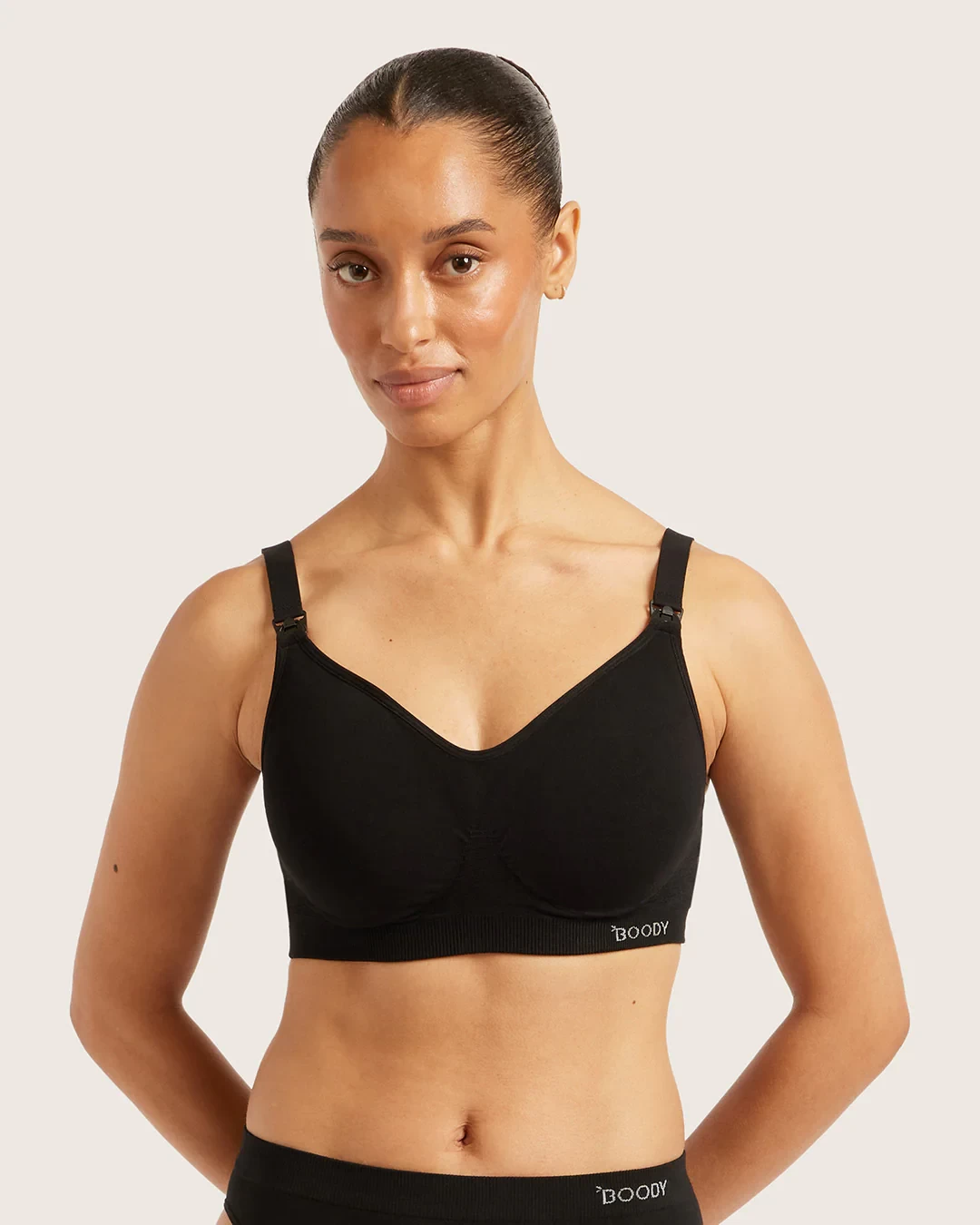 A woman wearing the Boody maternity bra in black, with her hands behind her back