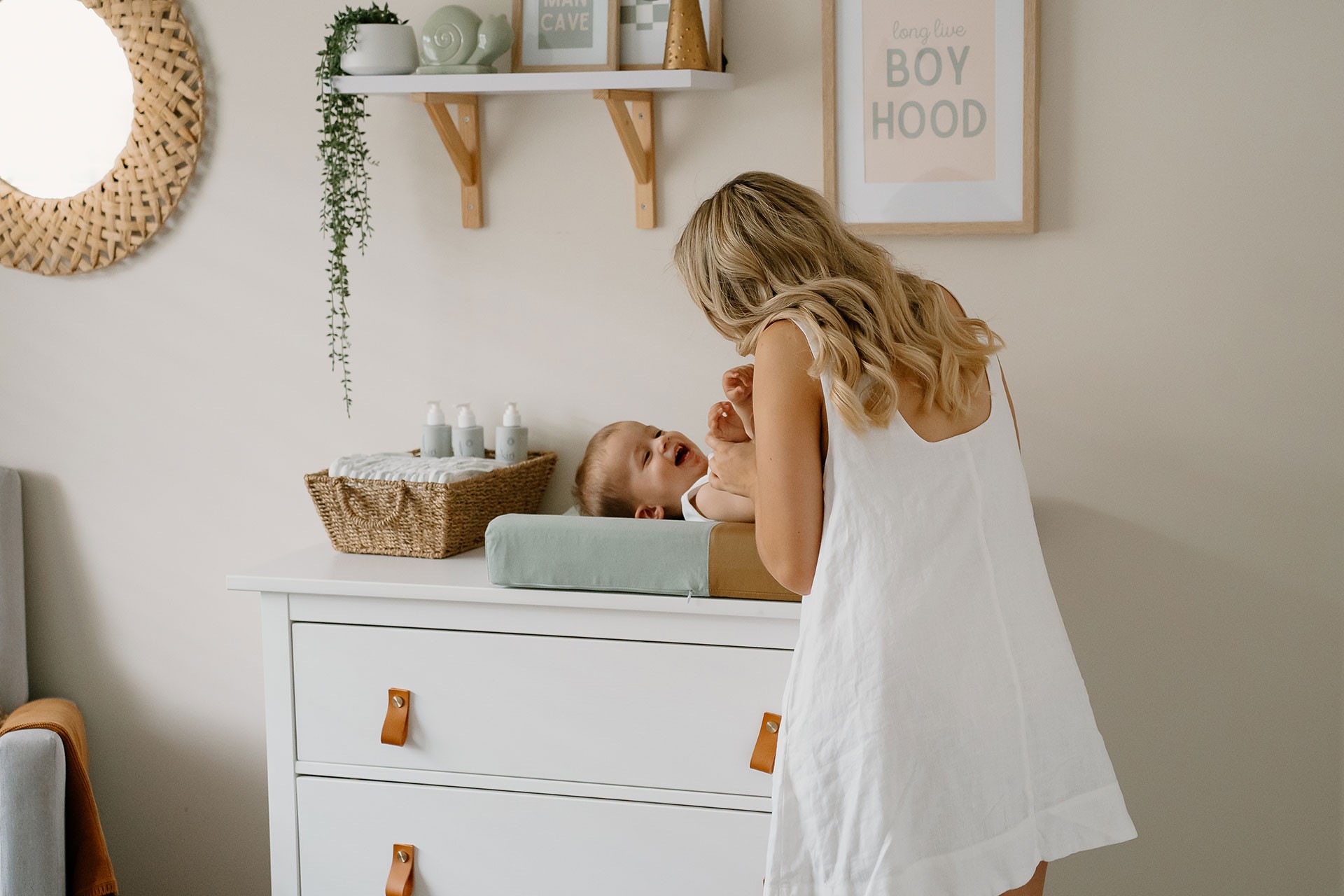 Baby lying on the best baby changing mat on top of a changing table in a kids bedroom as mum gently changes his diaper.