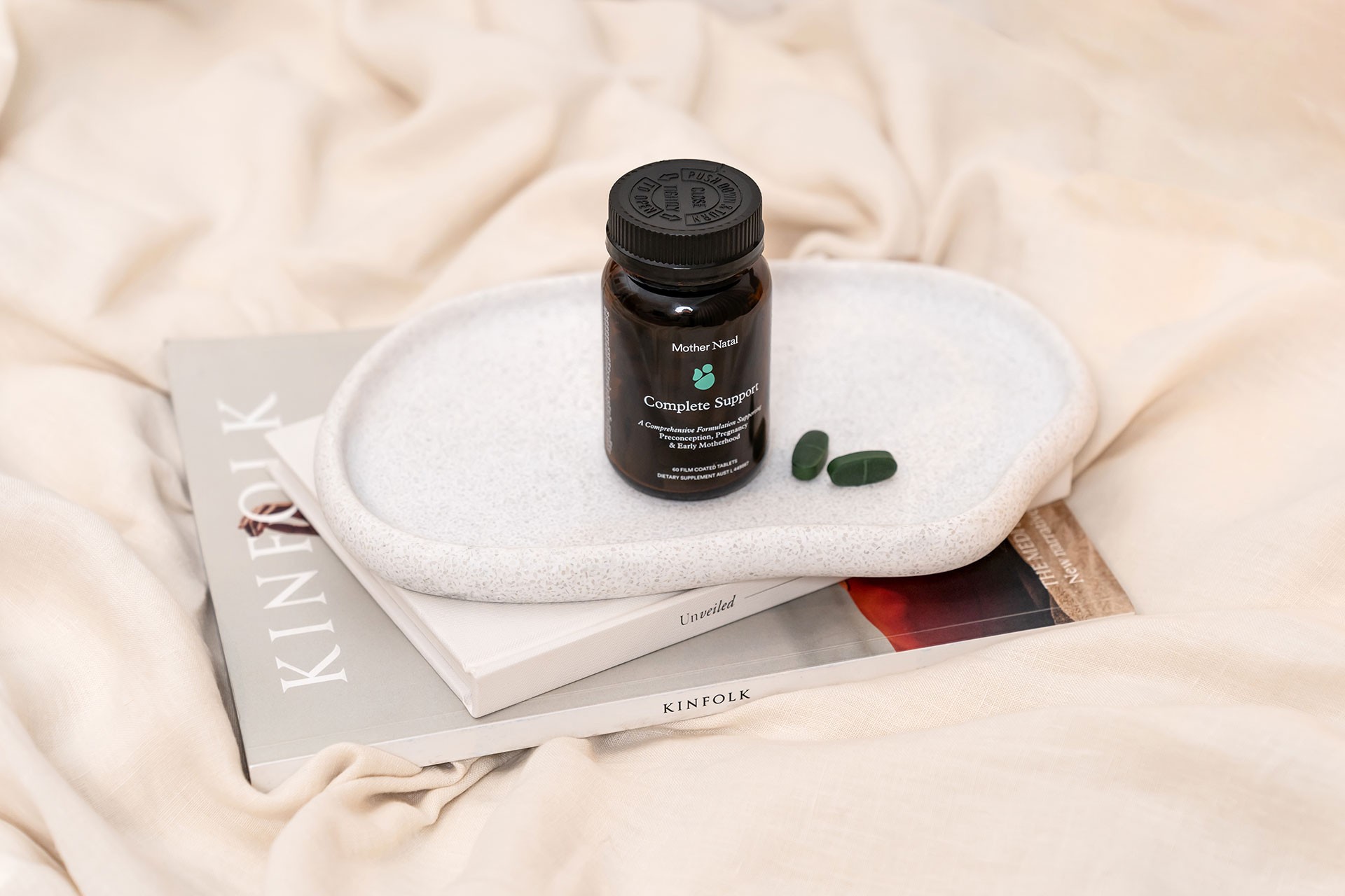 Pregnancy supplements bottle with two tablets on a white stone plate stacked on Kinfolk books – minimalist product styling
