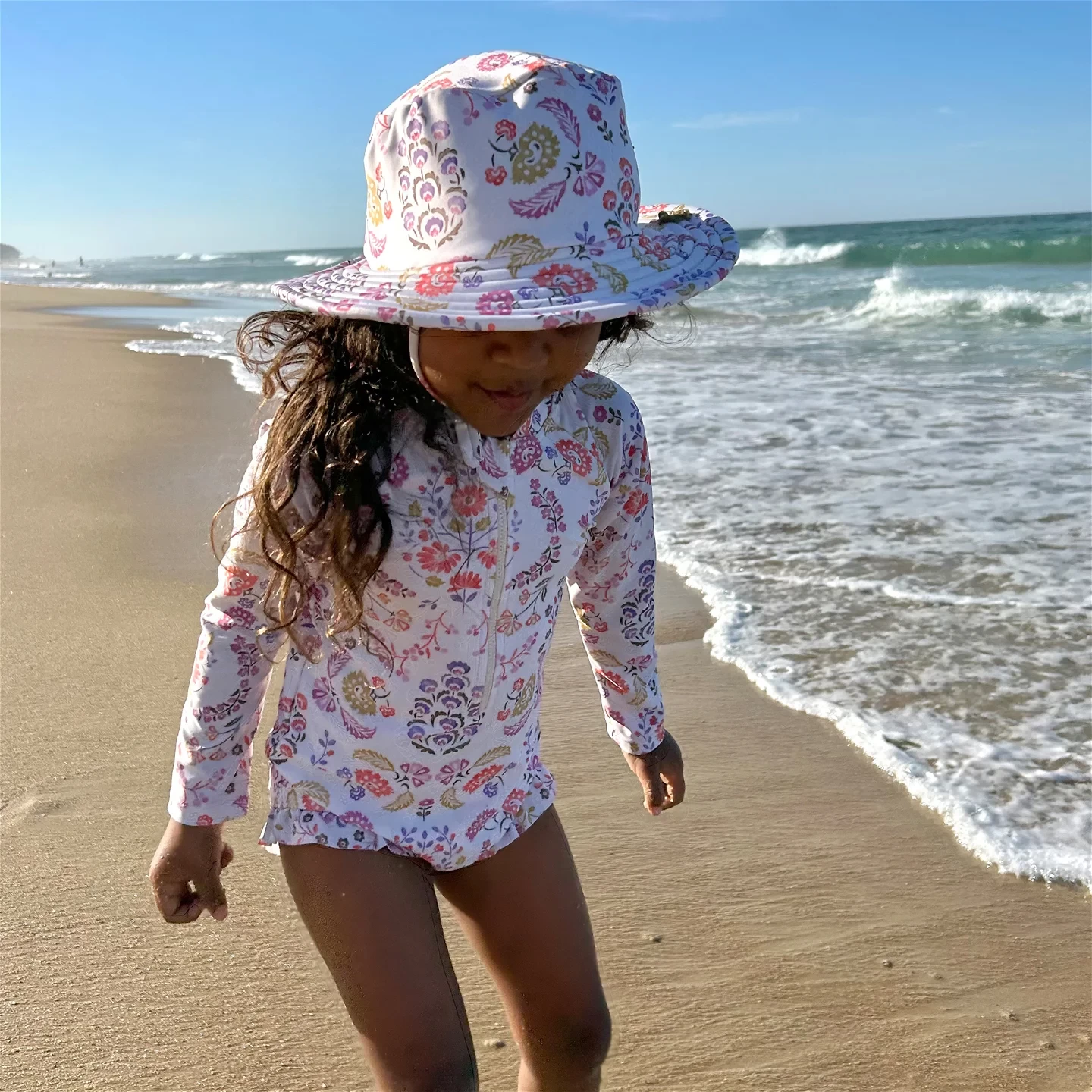 Girl walking beside the beach wearing purebaby best swimwear on a sunny day.