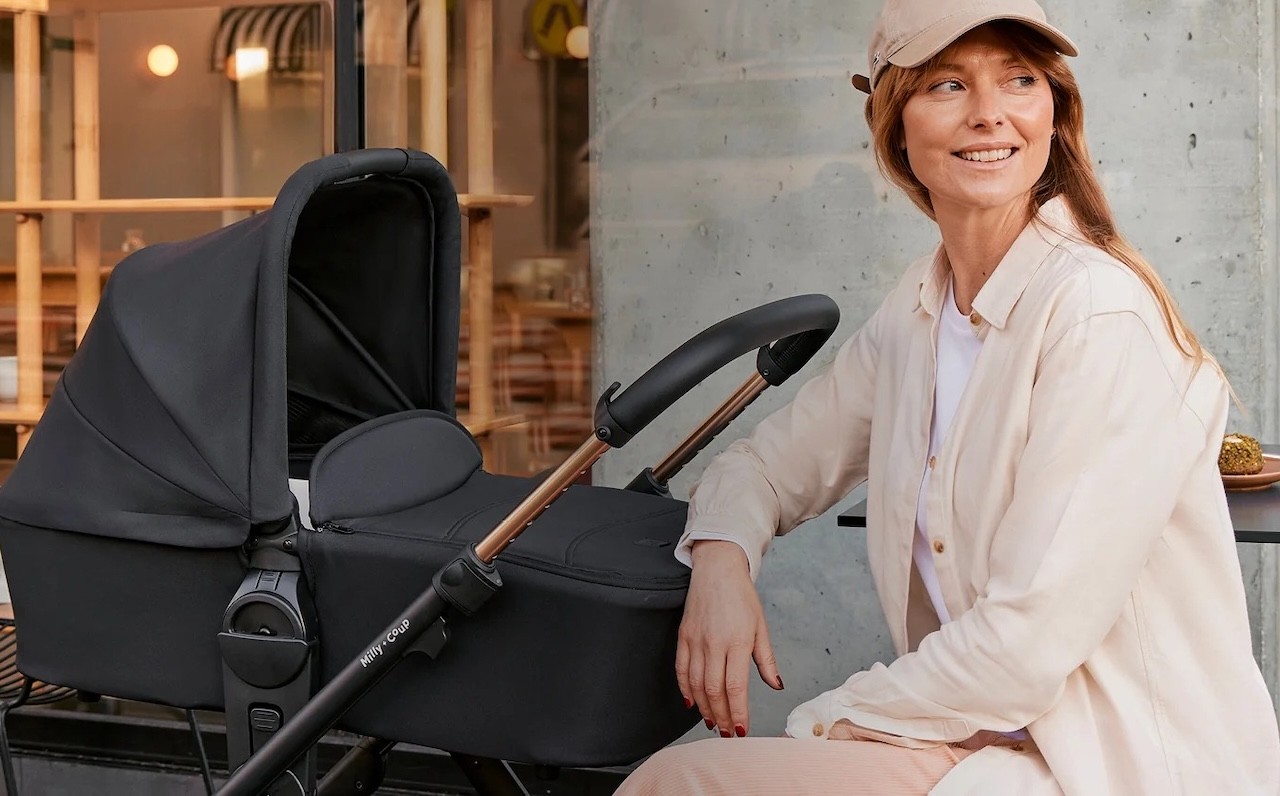 An Australian mum sitting at a cafe next to her Milly + Coup Milo2 pram
