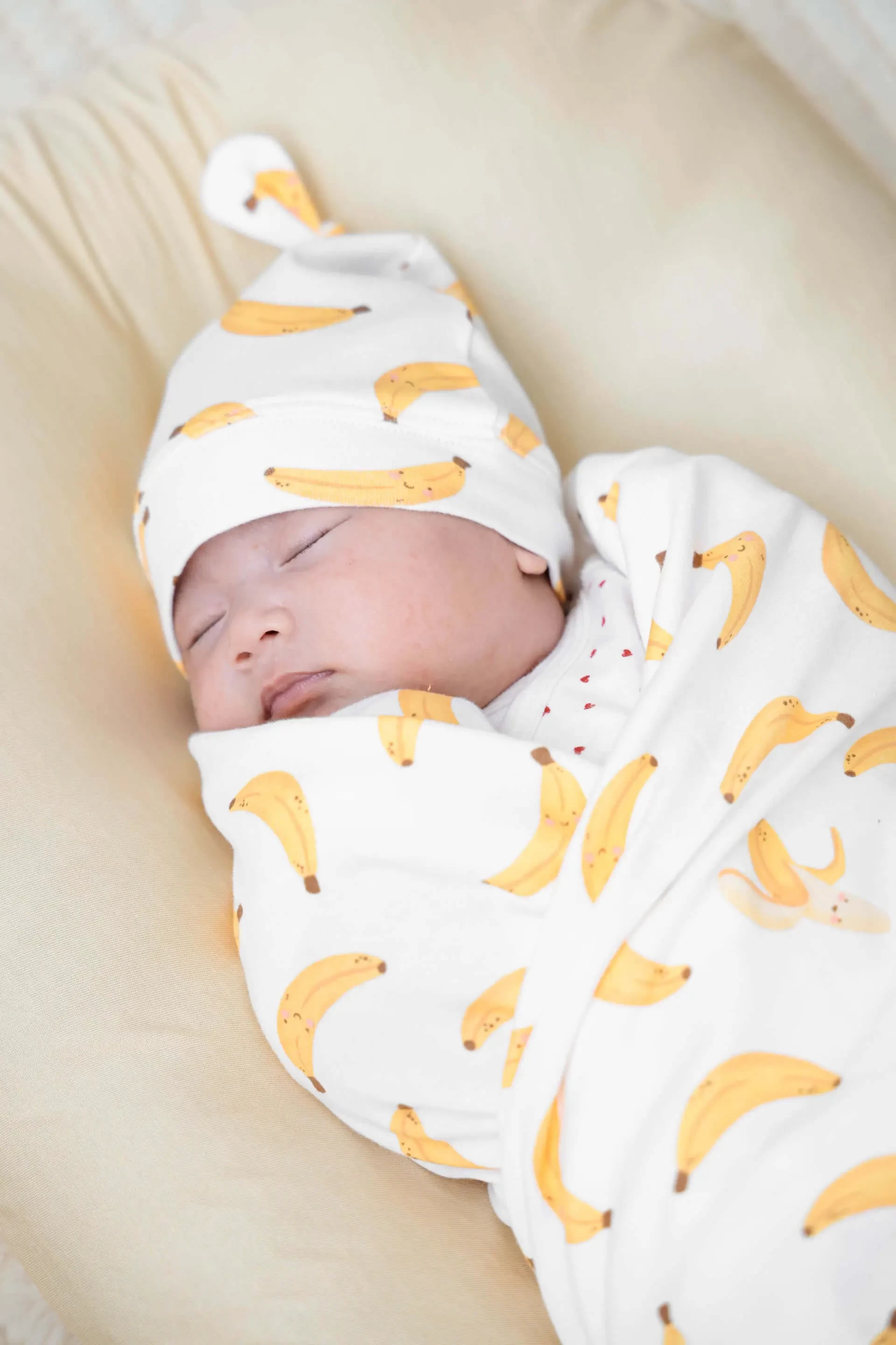 Baby wearing banana print swaddle and hat, one of the best baby clothes designed for snug and cosy sleep