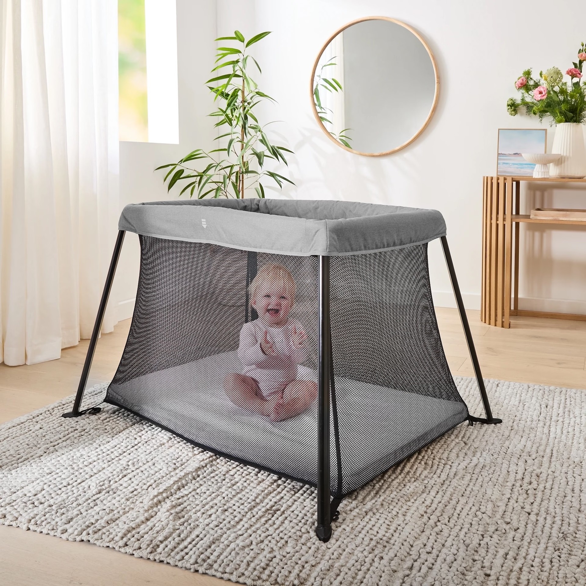 Kmart's Snooze Portacot, one of the best travel cots in Australia, with a toddler sitting in it in a lounge room
