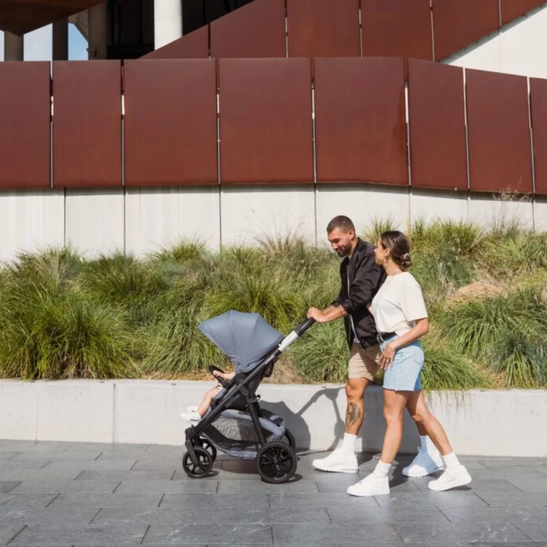 Couple pushing Redsbaby METRO³ Lite Stroller outdoors with their baby inside.