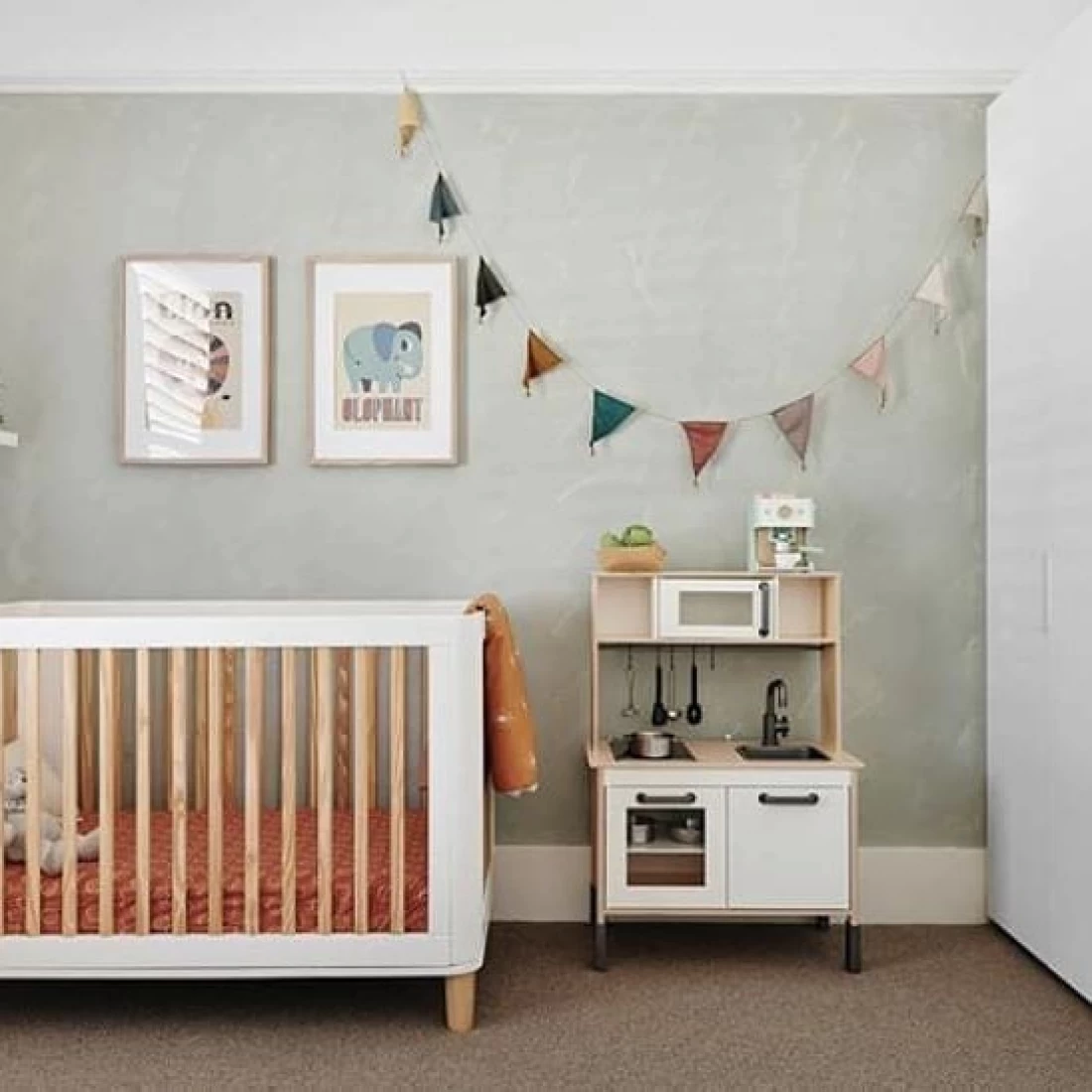 White crib with orange mattress and neutral tone wall decorated with bunting, showcasing the best baby boy nursery room decor ideas.
